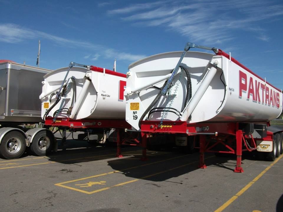 Two white and red Paktrans tanker trailers parked on a lot under a blue sky.