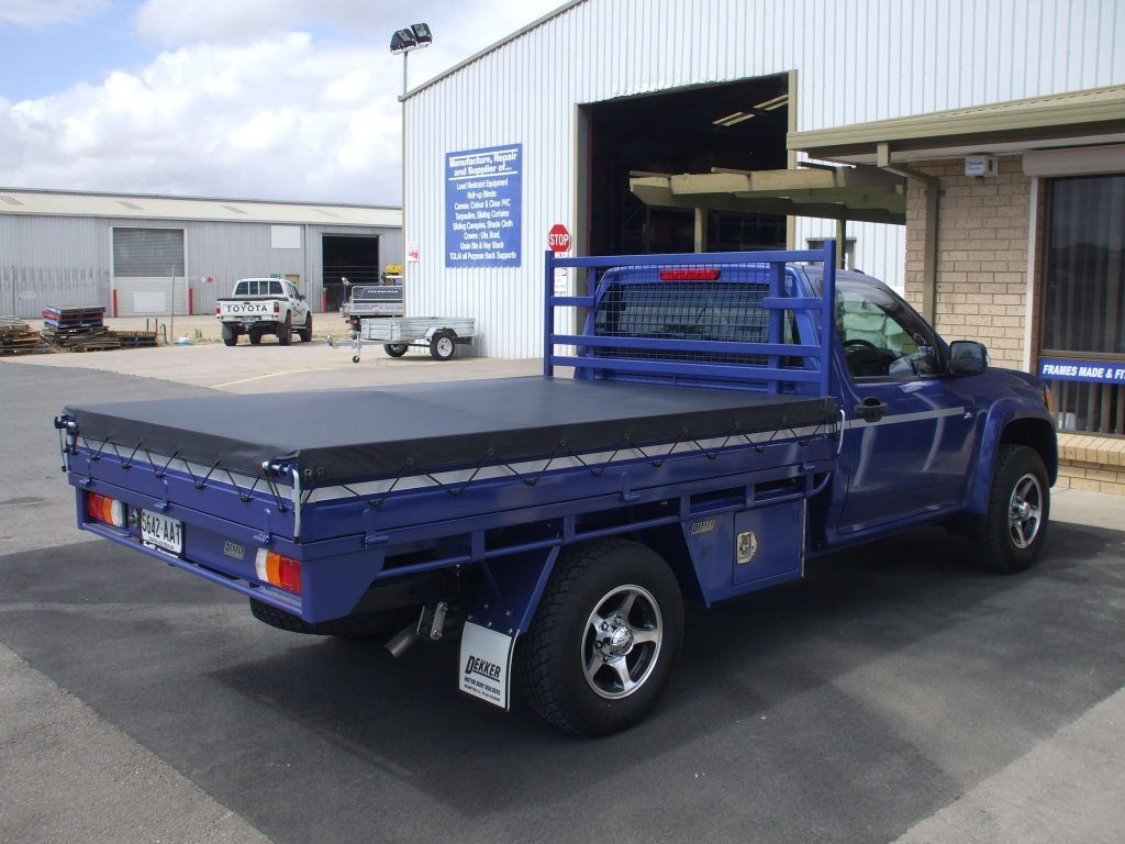 Blue pickup truck with flatbed and canopy parked in front of a building.