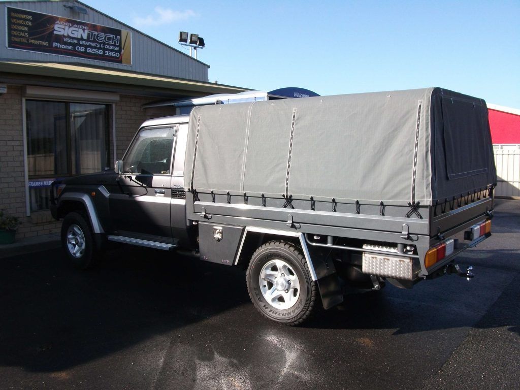 Dark gray pickup truck with a canvas cover parked outside a building.
