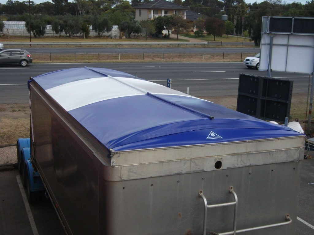 Trailer with blue and white canopy, parked near a road.