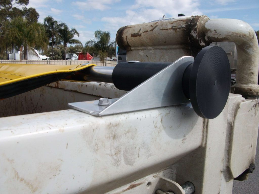 Metal bracket with black roller mounted on a dirty white truck.