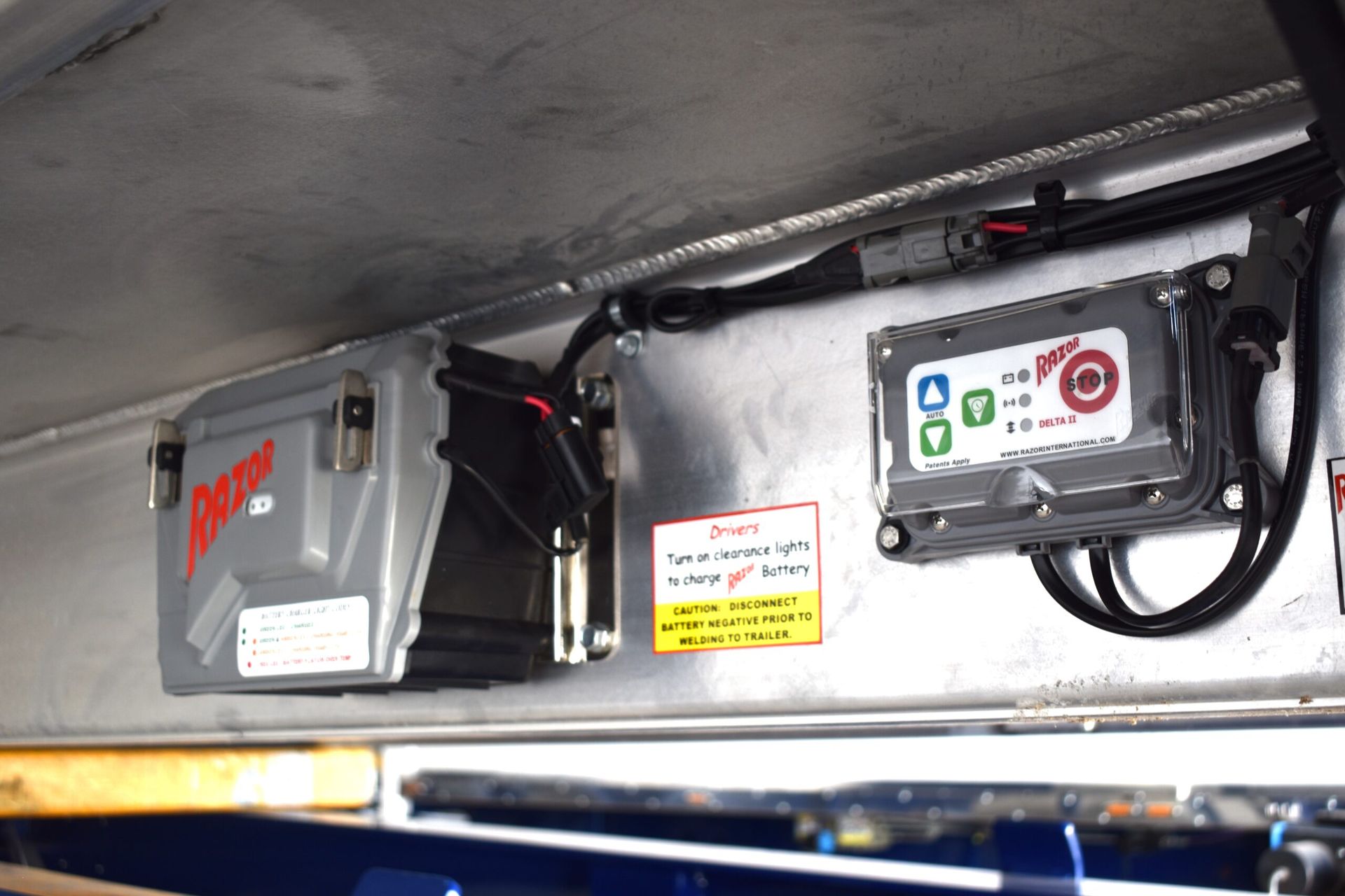 Mounted electrical control boxes and wiring under a vehicle roof panel, including a gray box with red logo and a black unit with labels.