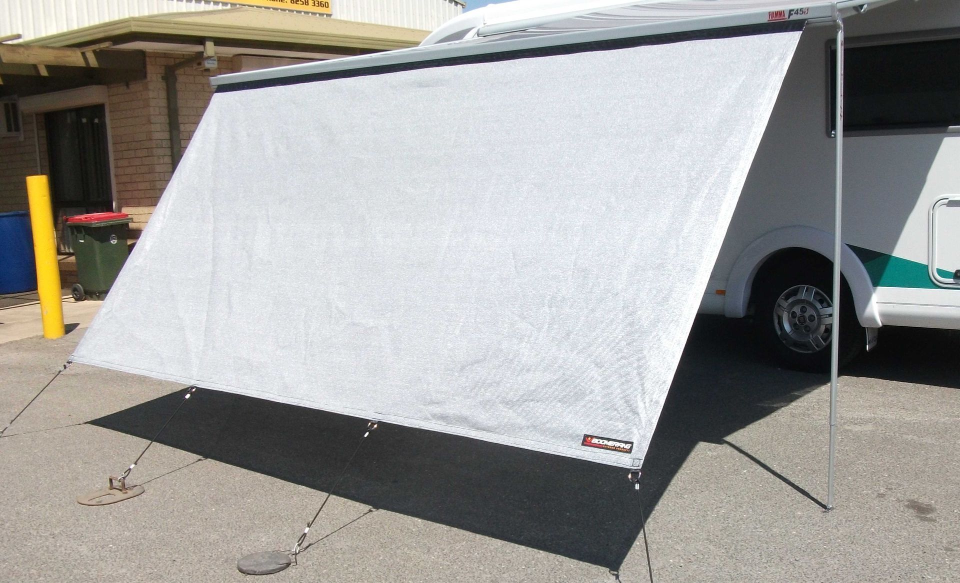 White campervan awning extended, creating shade; silver pole supports it, with tie-downs on the ground.