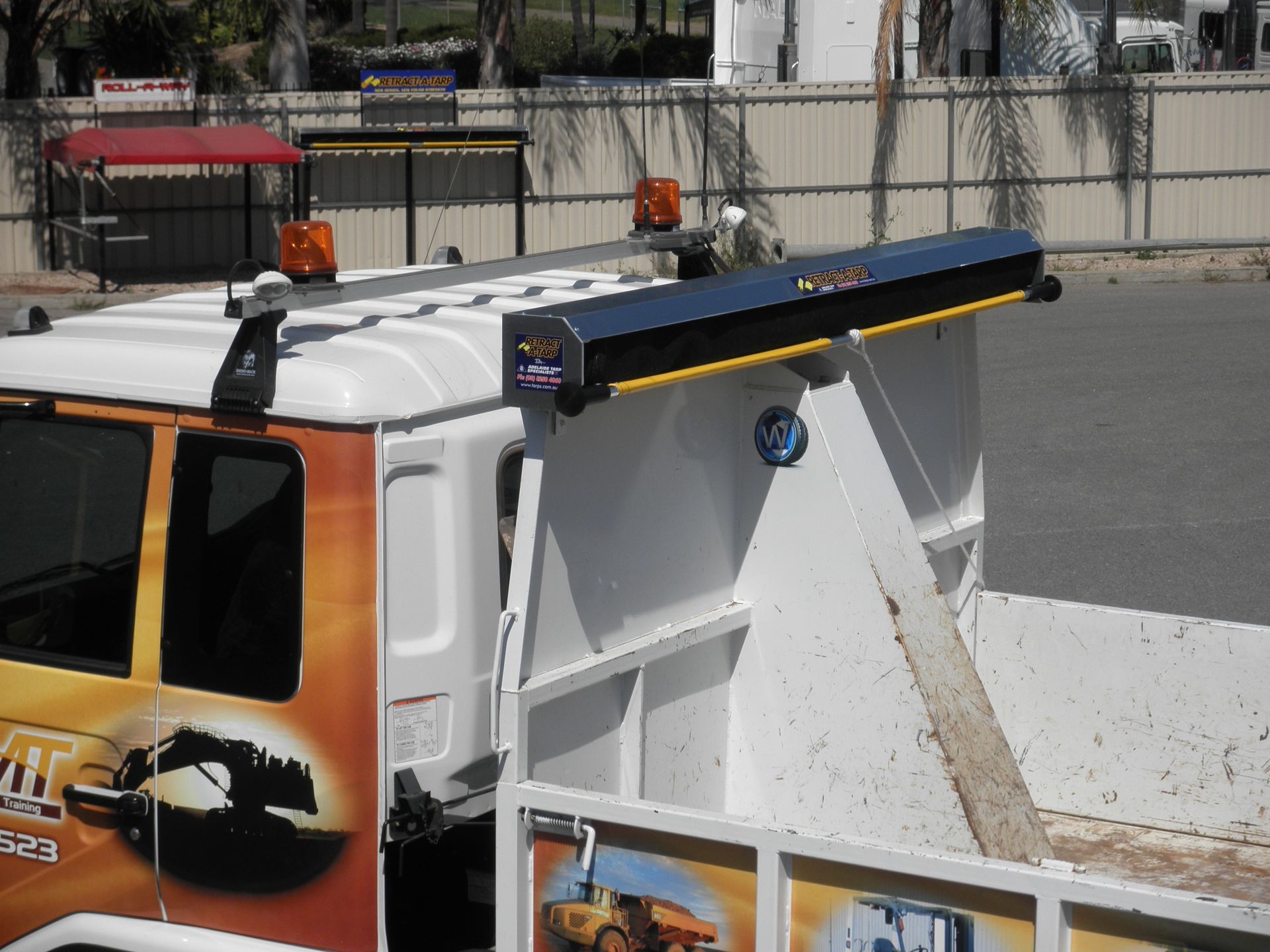 A white truck with an orange and black light bar on the roof, with graphics on the side.