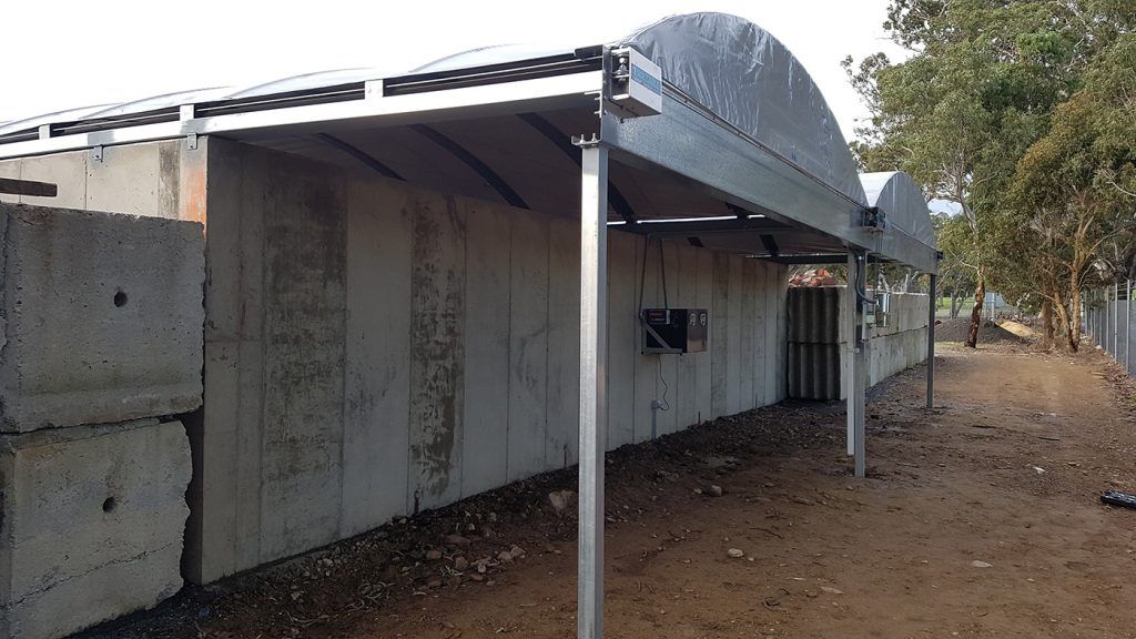 Greenhouse structure with concrete walls, metal roof, and arched plastic cover.