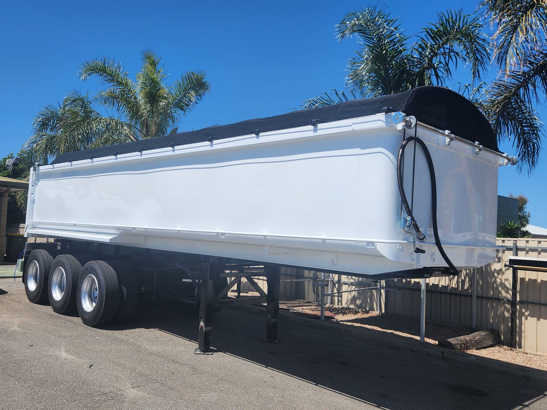 White semi-trailer with black cover, parked outdoors on a sunny day.