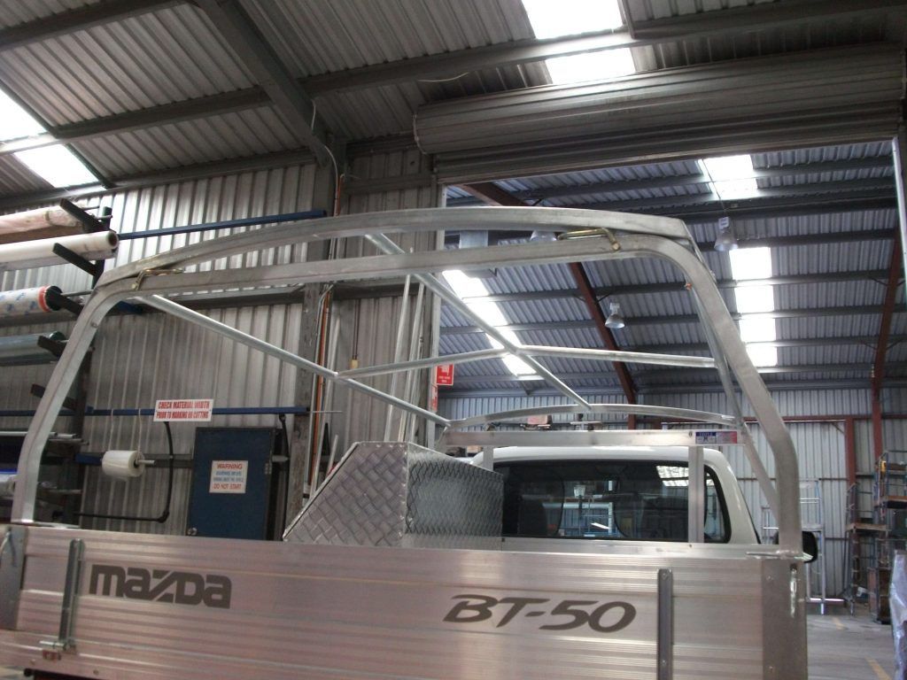 Aluminum roll bar frame on a Mazda BT-50 truck bed in a metalworking shop.
