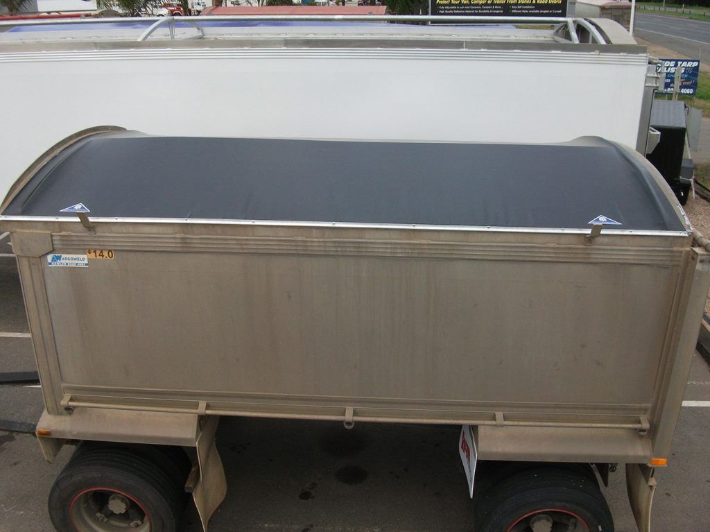 Tan utility trailer with a black tarp cover in a parking lot.