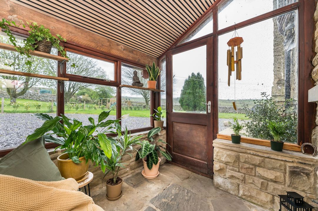 Sunroom with wood ceiling, potted plants, cushioned bench, and stone wall overlooking a green yard