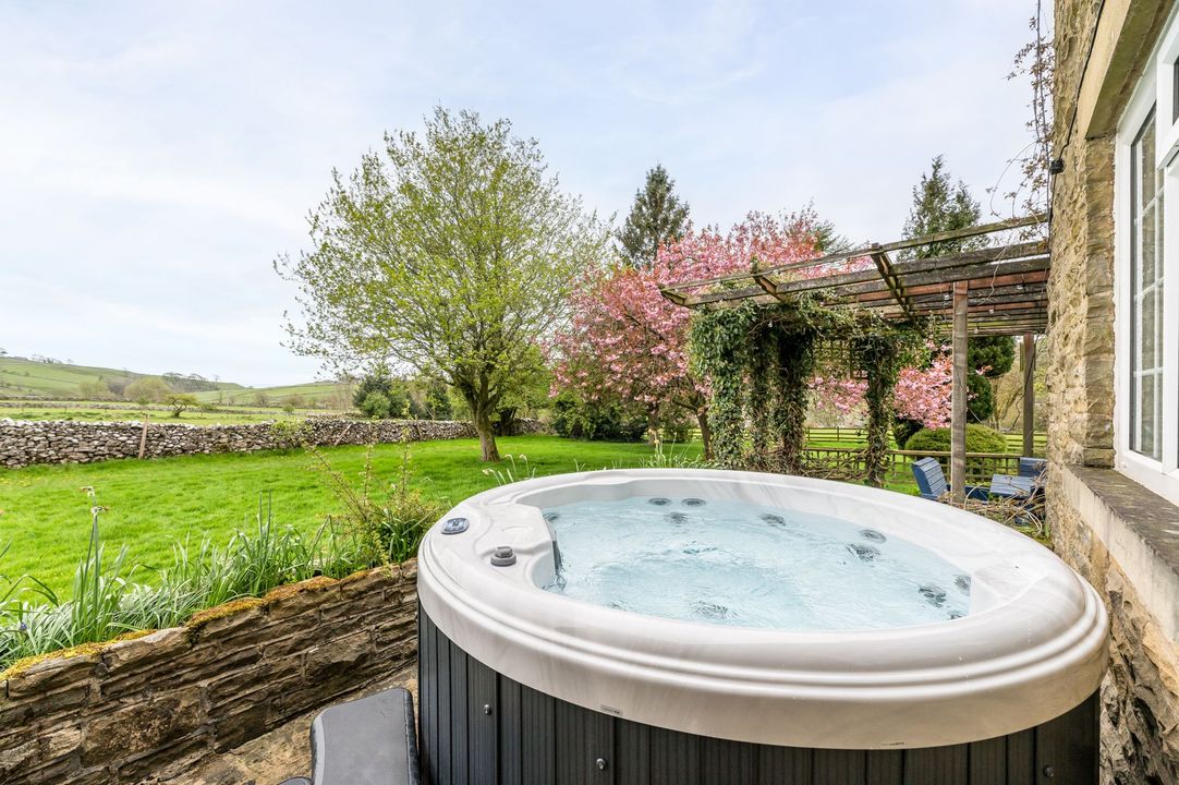 Hot tub on a patio overlooking a green field and blooming trees in a sunny garden