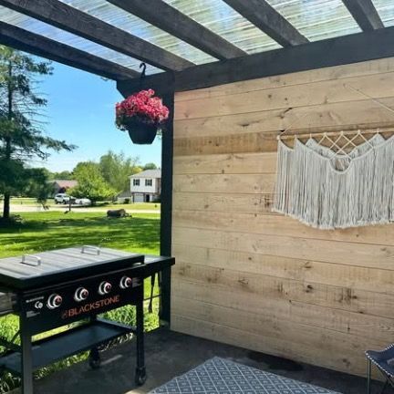 A Blackstone flat-top grill on a covered patio next to a wooden wall decorated with a white macramé wall hanging.