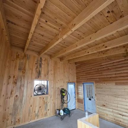 Interior view of a rustic room with light-colored knotty pine walls, exposed beam ceiling, a small window fan, and two doors.
