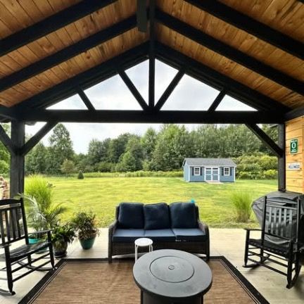 A covered porch with rocking chairs and a sofa facing a grassy backyard with a small shed under a cloudy sky.