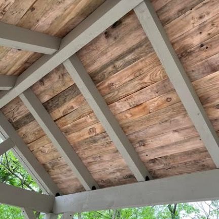 Angled view of a rustic wooden ceiling with natural grain planks set between gray painted structural beams.