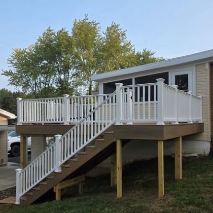 A brown composite deck with white railings and stairs leads up to a screened-in porch on the side of a house.