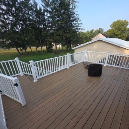 A spacious, elevated wooden deck with white railings, looking out toward a grassy yard and pine trees.