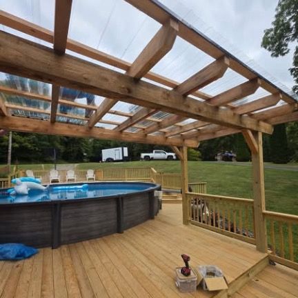 A wooden deck surrounding an above-ground pool, covered by a timber pergola with a clear, corrugated roof.