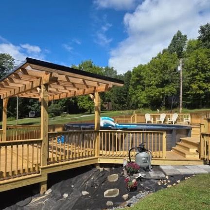 A wooden deck with a pergola surrounding an above-ground pool, with patio furniture visible in a sunny, grassy backyard.