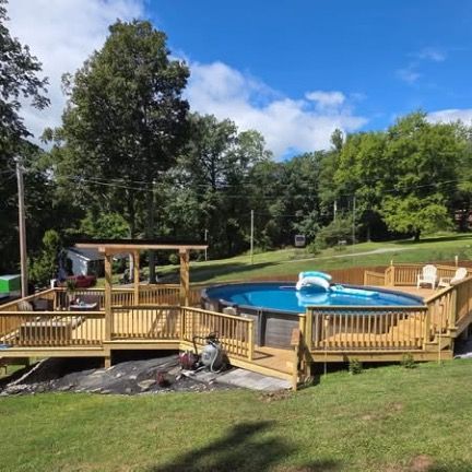 A large, multi-level wooden deck surrounding an above-ground swimming pool in a grassy backyard with trees.