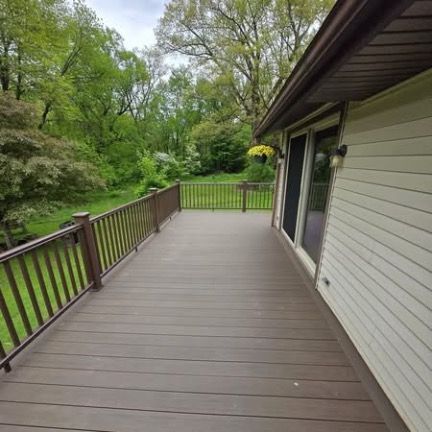 A view of a modern brown composite deck with a metal railing, overlooking a lush green wooded backyard.