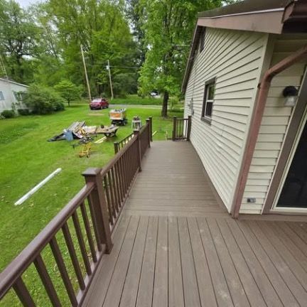 A deck with brown composite railings and floorboards attached to the side of a house overlooking a grassy backyard.