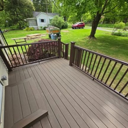 A wide, dark brown deck with a matching railing overlooks a grassy backyard with trees, a small shed, and a red car.