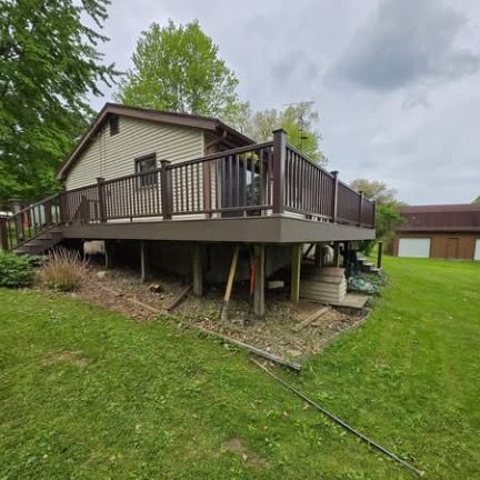 A side view of a house featuring a large, elevated deck with dark brown railings, situated in a green, grassy yard.