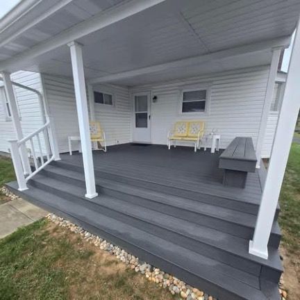 A dark gray deck with matching stairs and bench, featuring white railings and pillars in front of a white house.