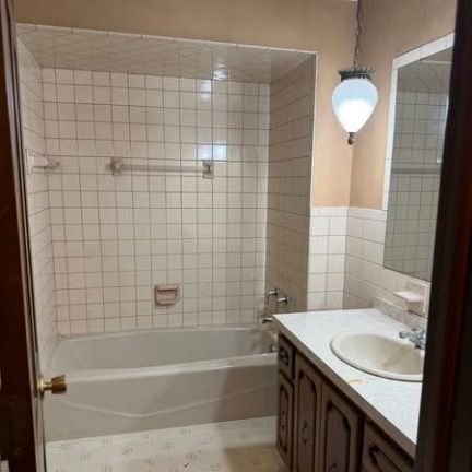 A bathroom with a white tiled tub and shower enclosure, a vanity with a white countertop and sink, and a pendant light.