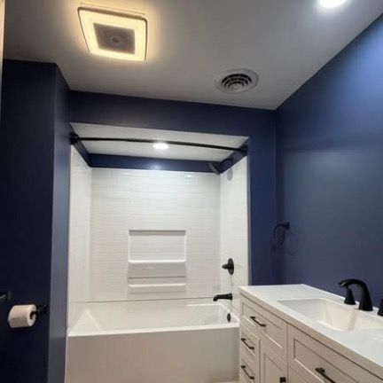 A modern bathroom featuring dark blue walls, a white tub and shower surround, white vanity, and black hardware.