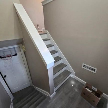 A staircase with gray wood-look treads and white risers next to a door with a small basketball hoop and a brown cardboard box.