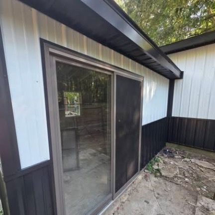 A view of a sliding glass door with a screen on a home exterior featuring white and dark metal siding.