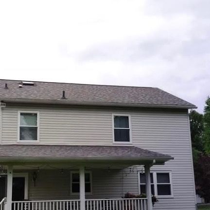 A two-story light gray house with vinyl siding, a shingled roof, and a covered front porch under a cloudy sky.