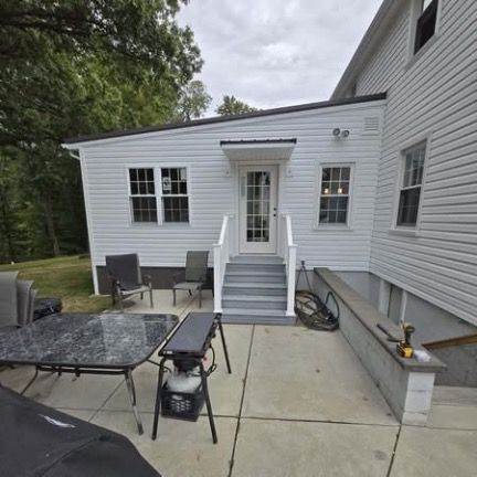 White house exterior with a patio, grey steps, a glass-paned door, and patio furniture on a concrete slab.