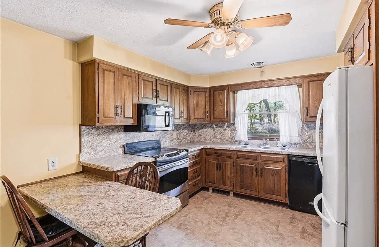 Compact kitchen with wooden cabinets, black appliances, and a window over the sink