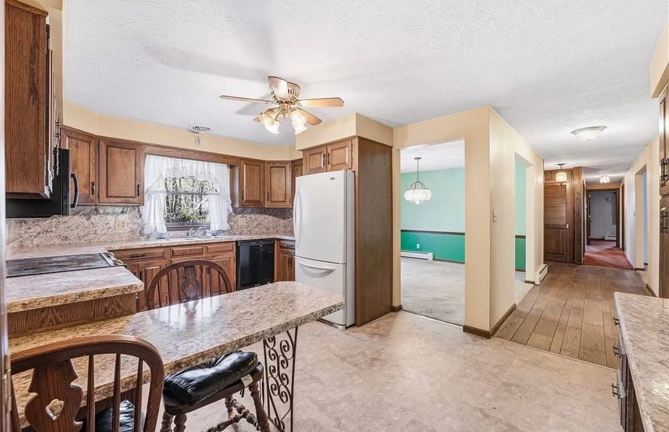 Kitchen and hallway in a home, with wood cabinets, granite counters, white fridge, and beige carpet.
