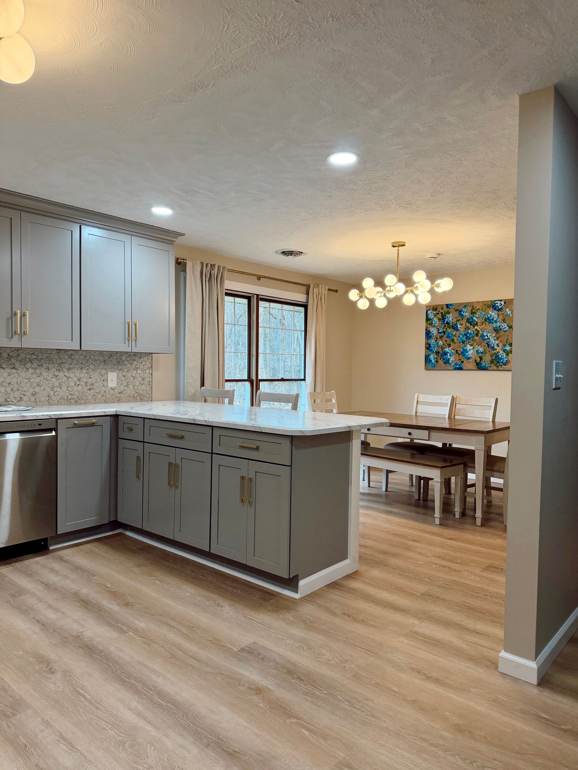 Bright modern kitchen and dining area with gray cabinets, light wood floors, and a chandelier.