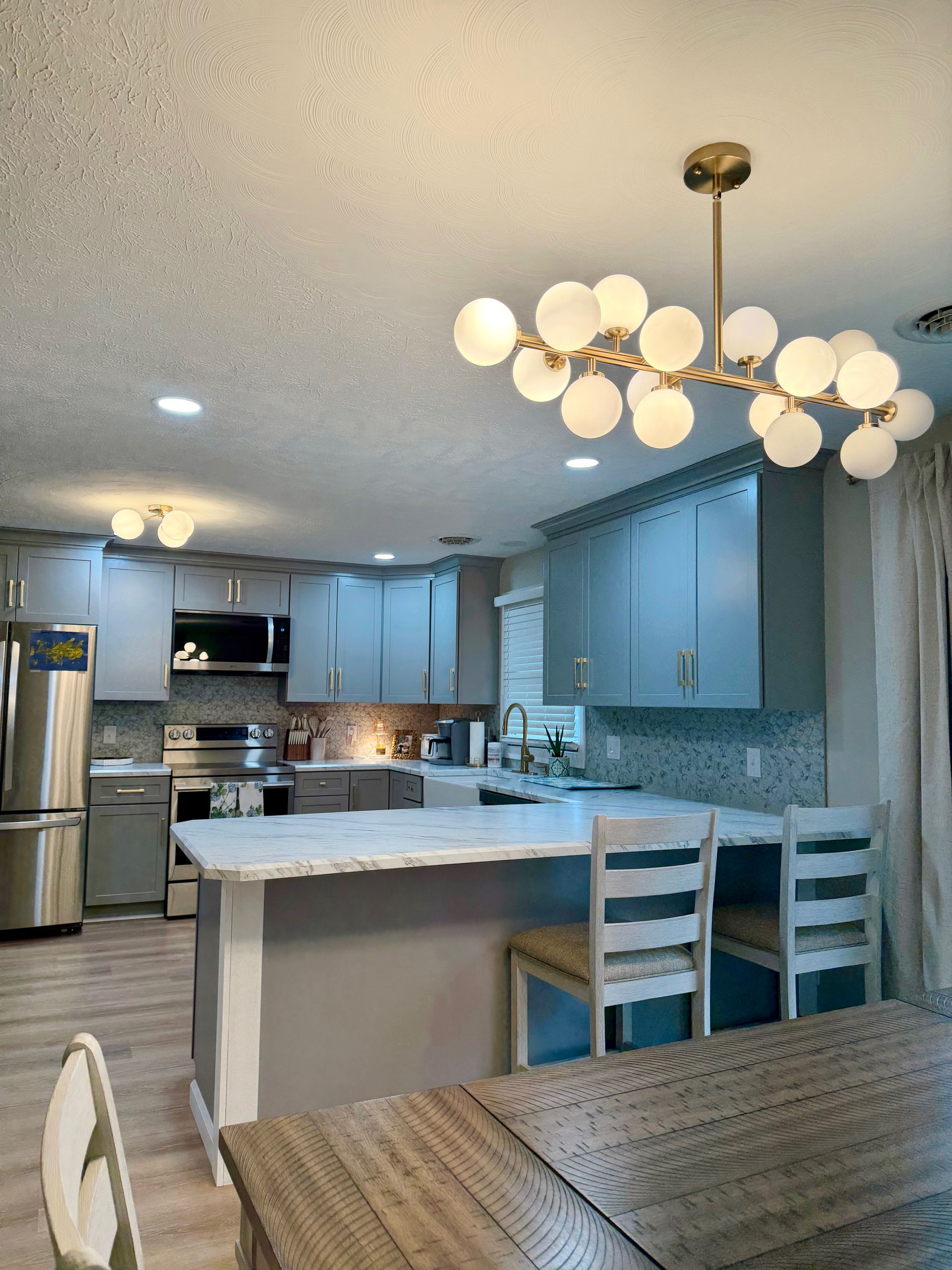 Bright modern kitchen with white cabinets, island, stainless appliances, and round chandelier above dining table