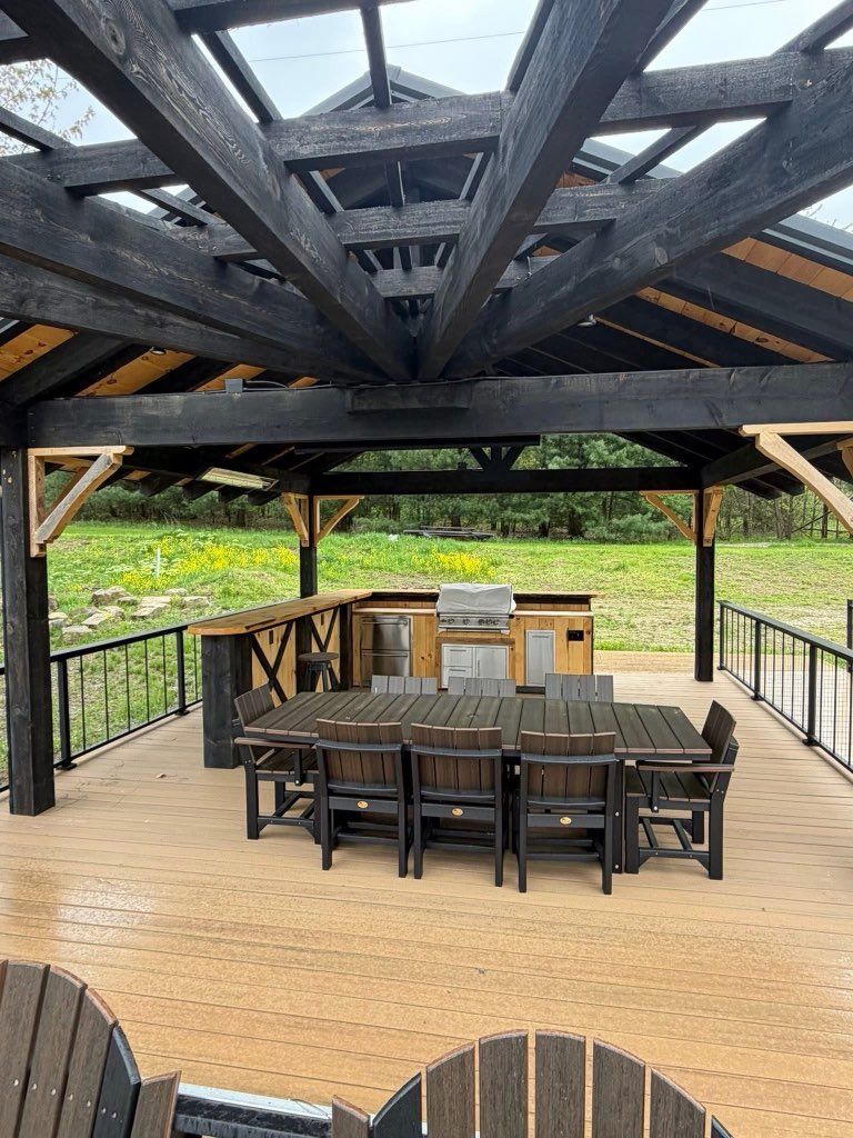Covered outdoor patio with dining table, chairs, and grill on a wooden deck overlooking a grassy area