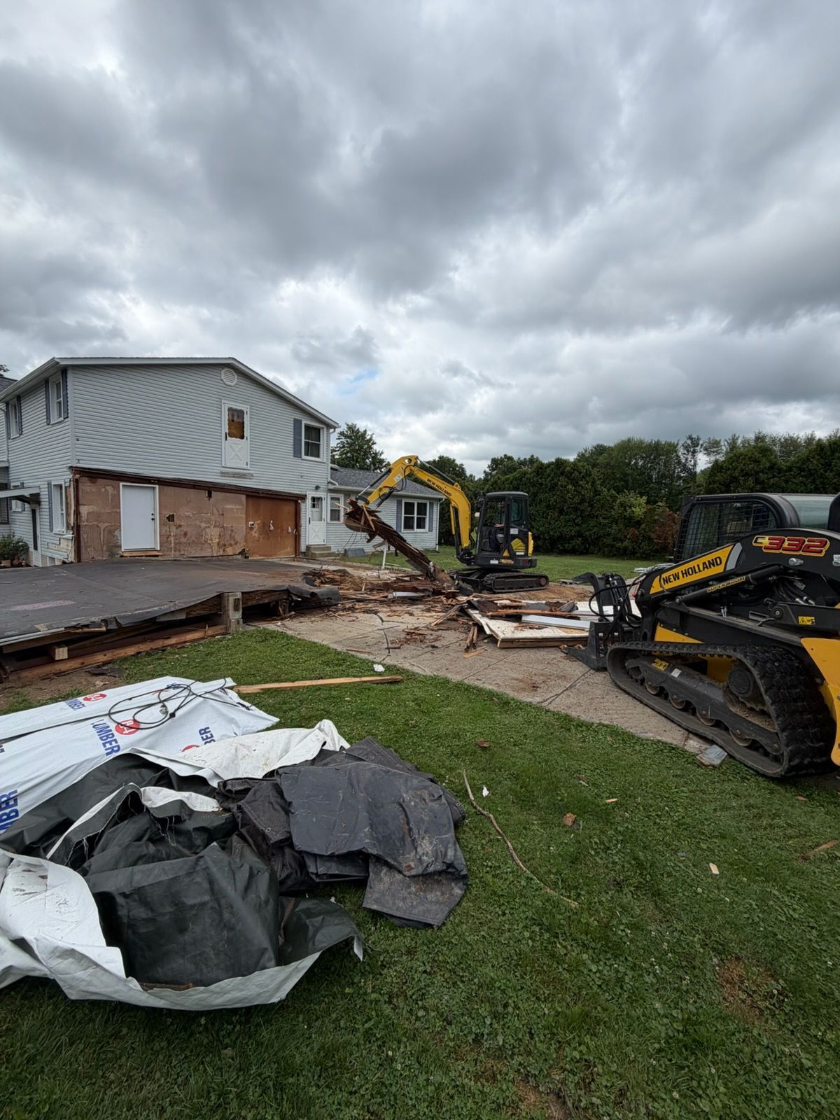 Excavator bucket dumping debris into a red dumpster outdoors among trees