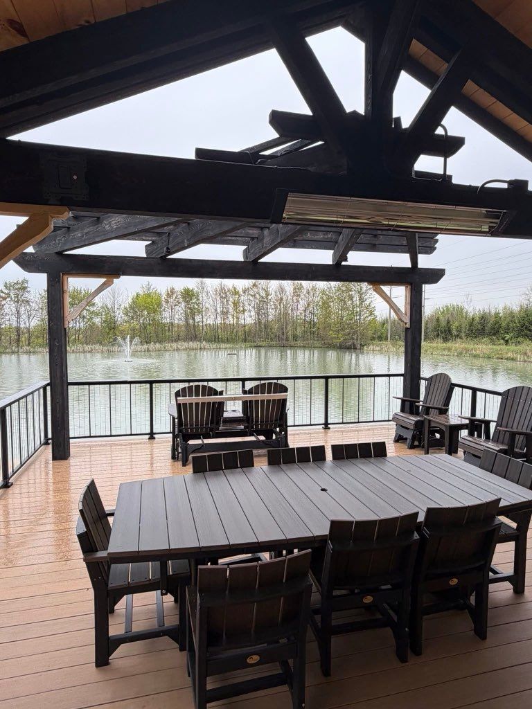 Covered lakeside deck with dark wooden dining tables, chairs, and a view of the water beyond the railing