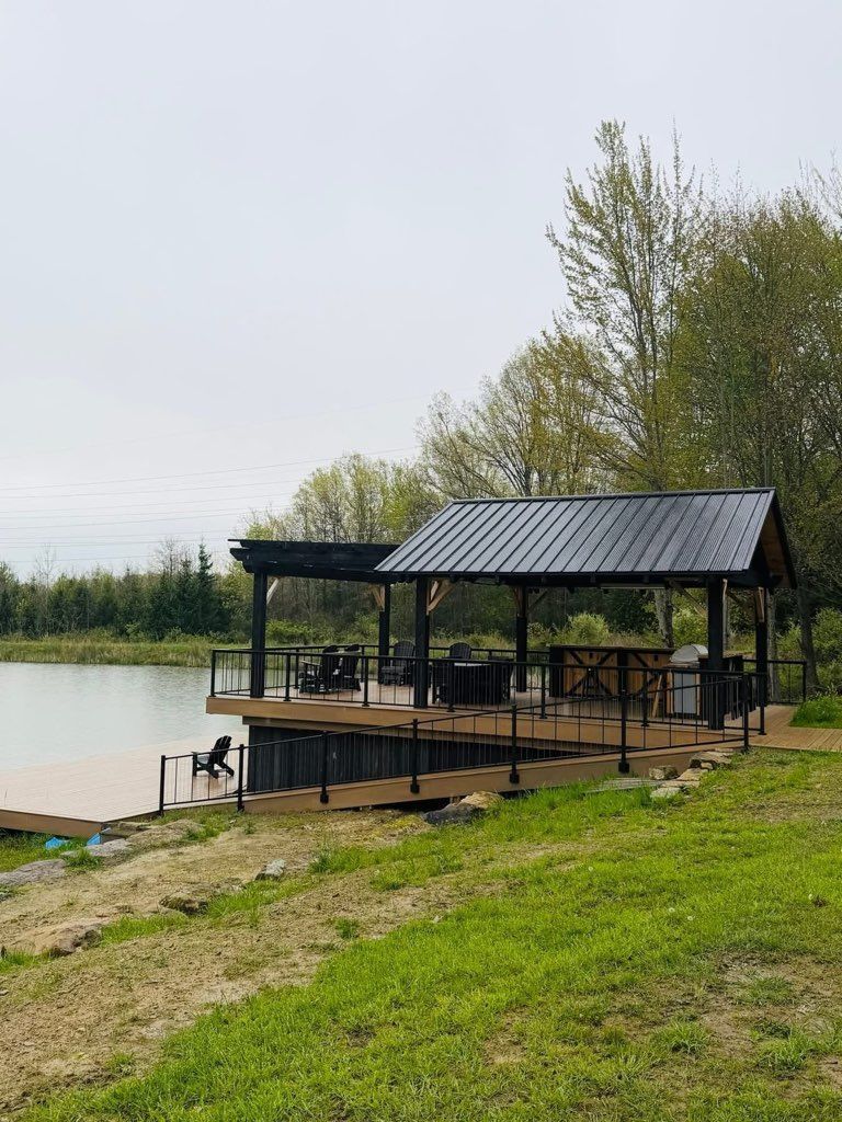 Covered lakeside dock with black roof beside calm water and grassy shore