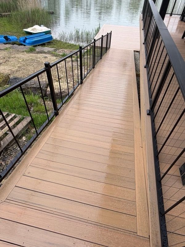 Wooden dock ramp with black railings leading to a calm lake shoreline