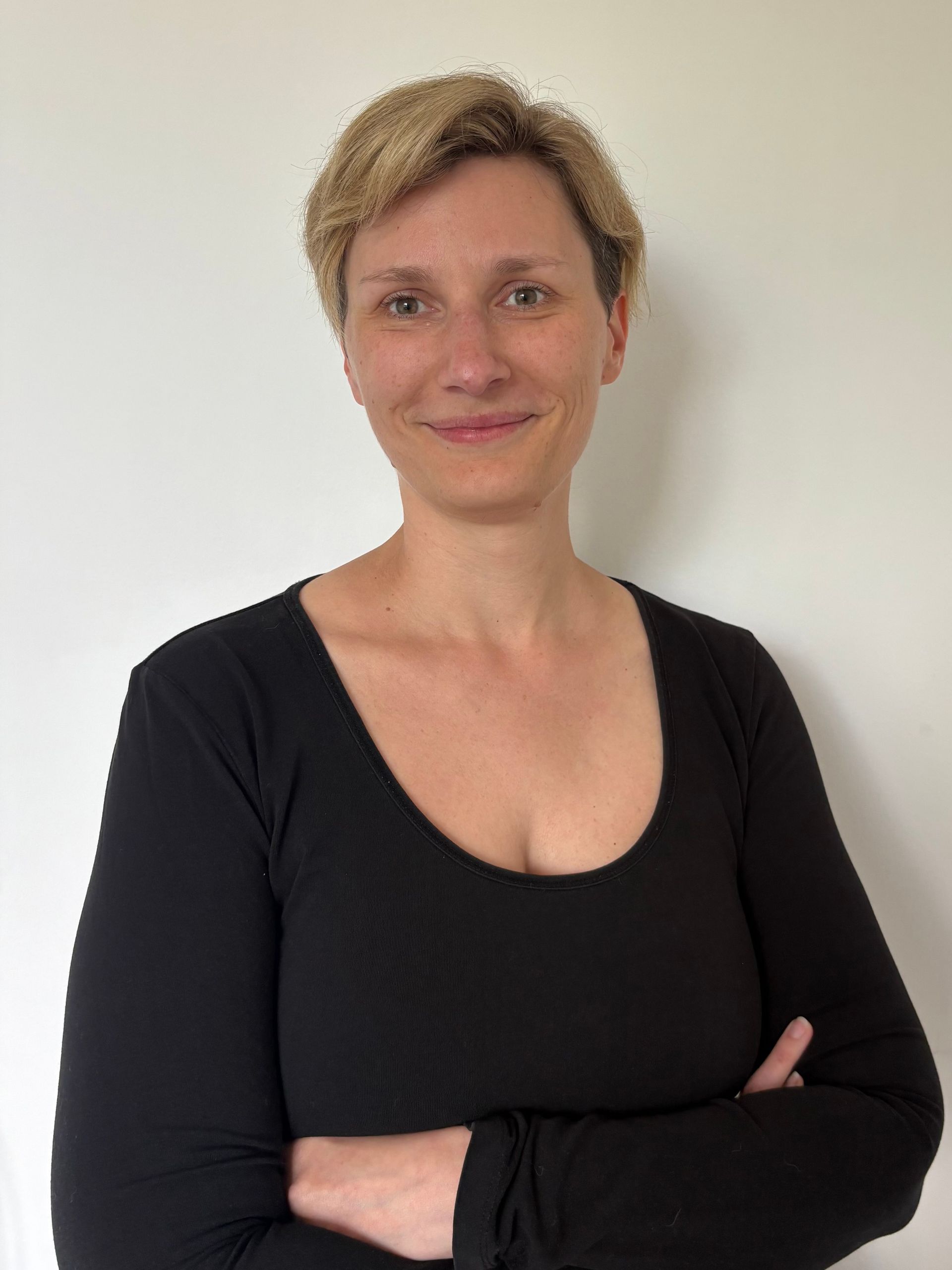 Eine Frau mit Brille und grauem Kapuzenpullover lächelt in die Kamera.