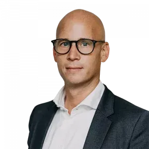 Ein kahlköpfiger Mann mit Brille und Anzug steht vor einem weißen Hintergrund.