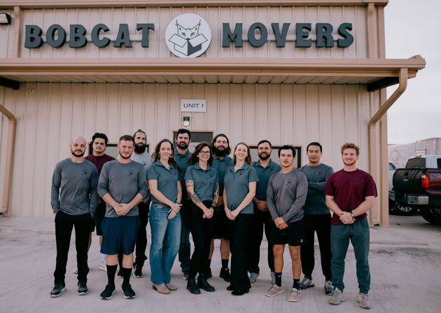 A group of people are posing for a picture in front of a bobcat movers building.