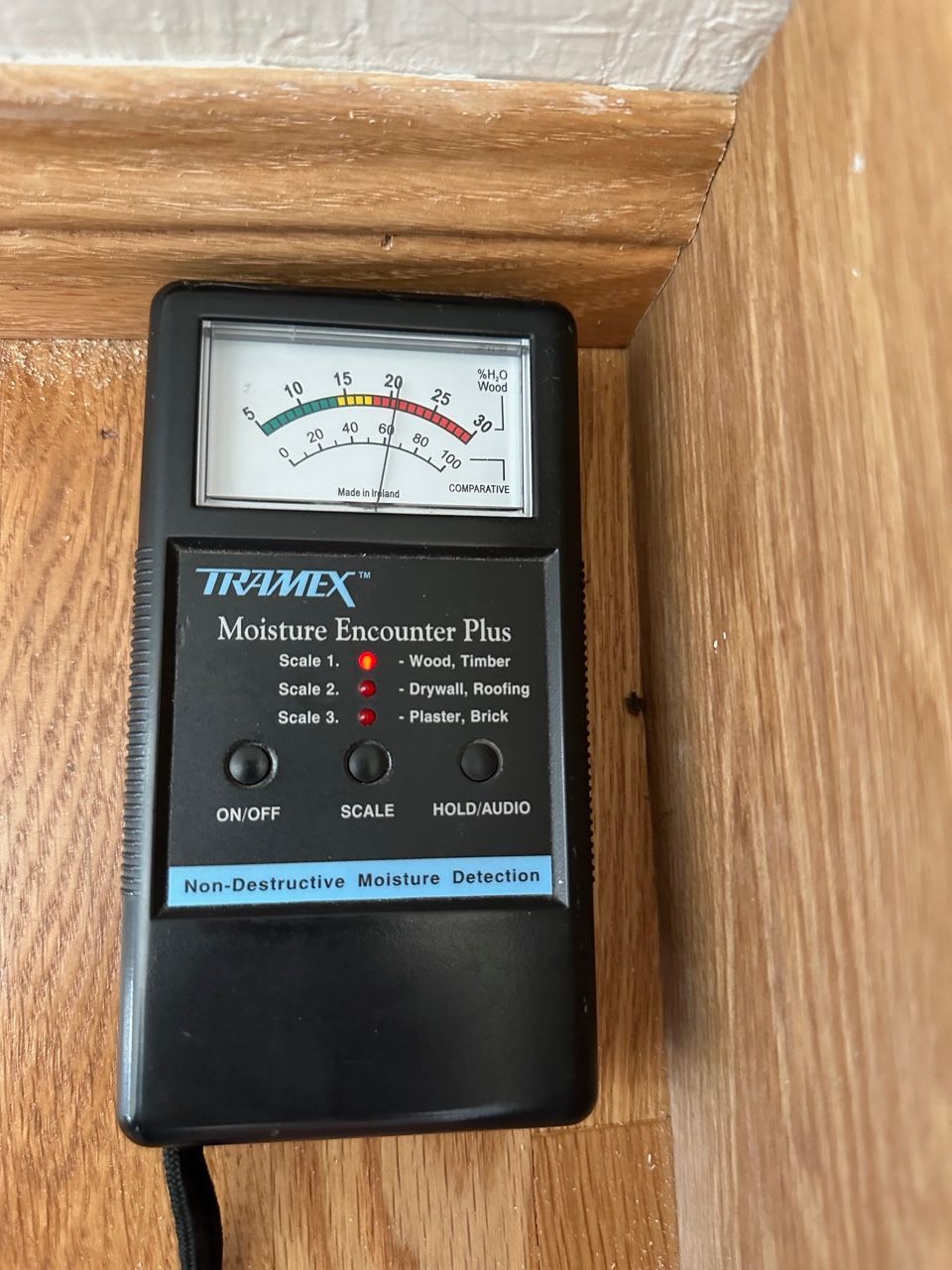 Moisture meter reading high on wood trim; the meter is black with a needle gauge.