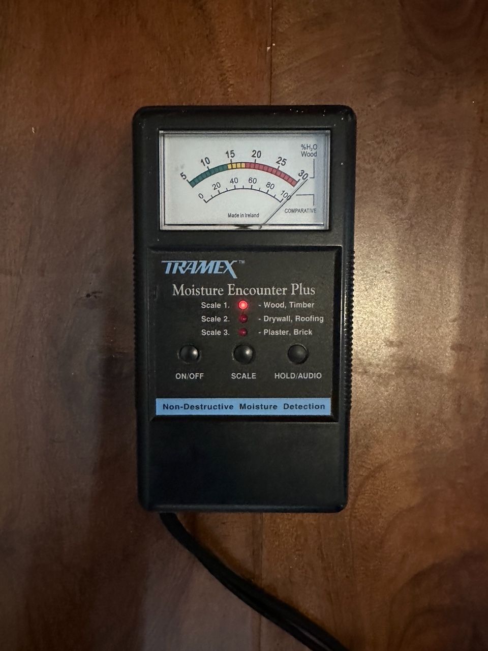 Black moisture meter on wood, with a gauge showing a reading of approximately 40.