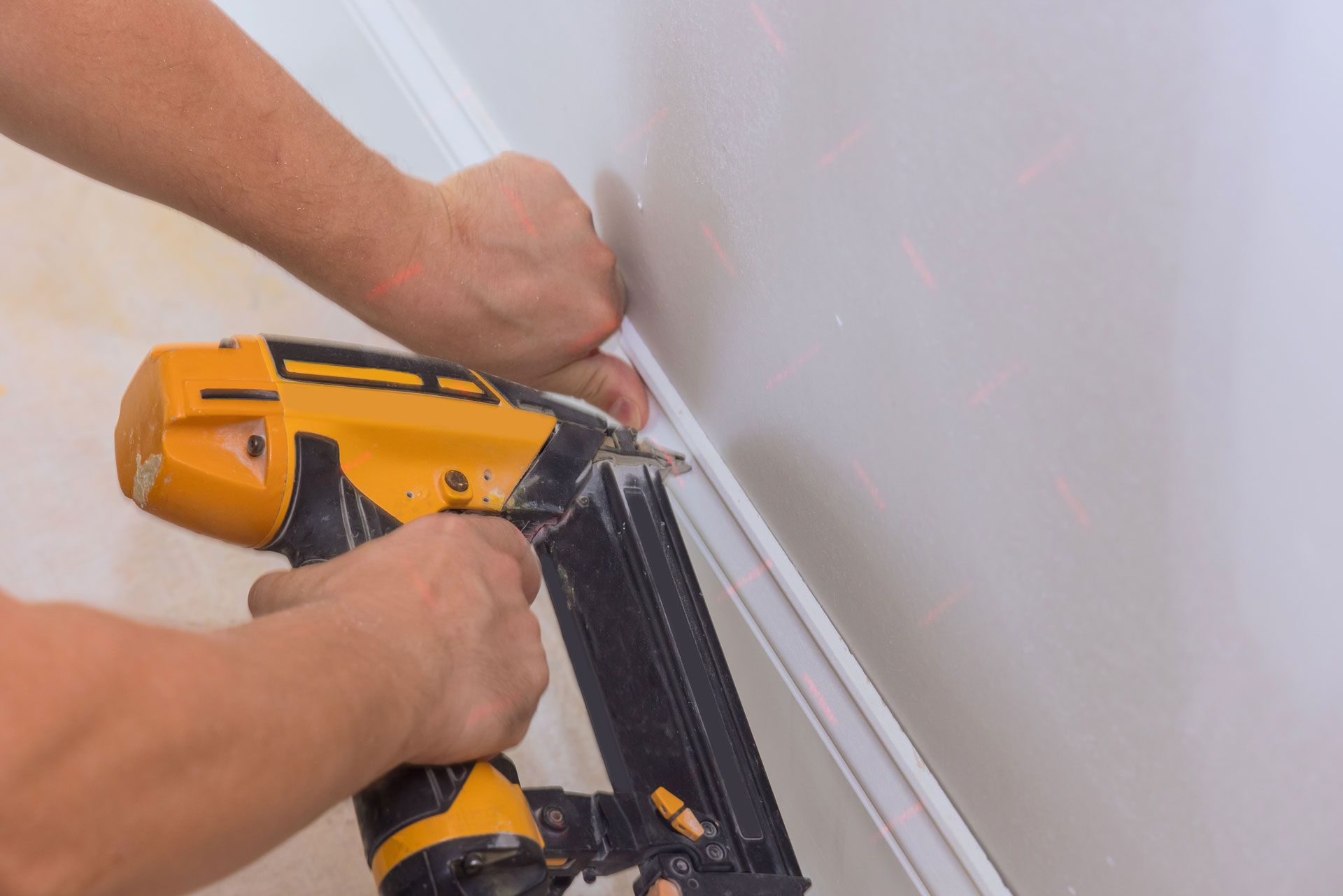 Person installing white molding on a white wall with a nail gun.