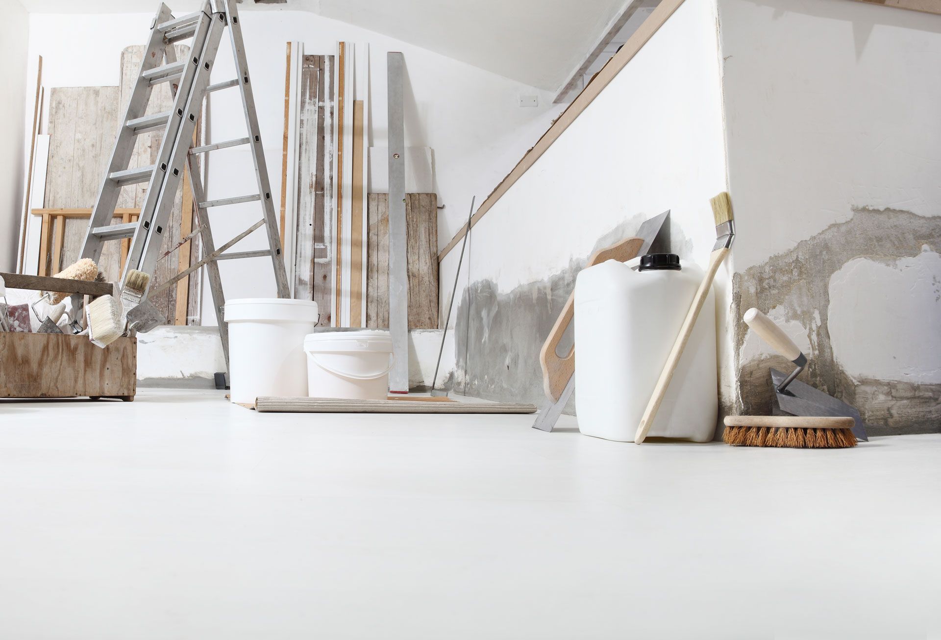 Room undergoing renovation, with ladder, buckets, and tools against a white wall and floor.